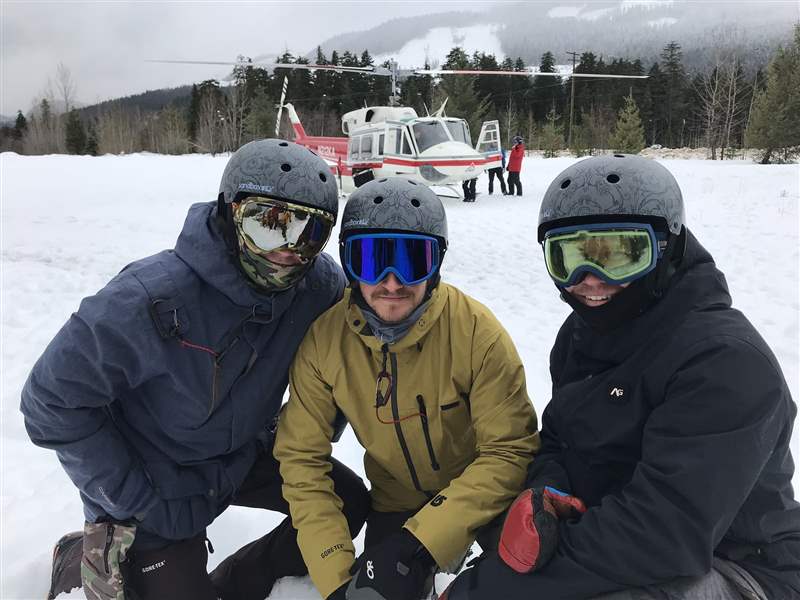 三名男子在雪中，背景中有一架直升机